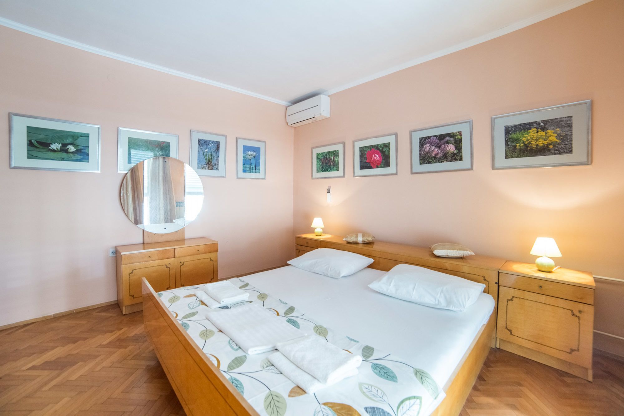 A bedroom with a bed, two bedside tables, a mirror, and framed pictures on the wall.