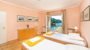 A hotel room with two beds, a wooden dresser, a view of the sea, and framed pictures on the wall.