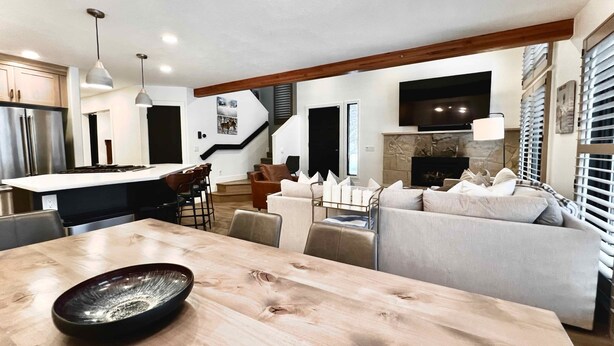 A modern kitchen with a central island, a dining area with a wooden table, and a living room with a sofa and fireplace.