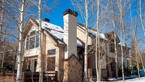 A two-story house with a stone facade, a chimney, and a snow-covered roof.