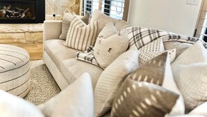 A cozy living room with a beige sofa adorned with various pillows, a fireplace, and a stone wall.