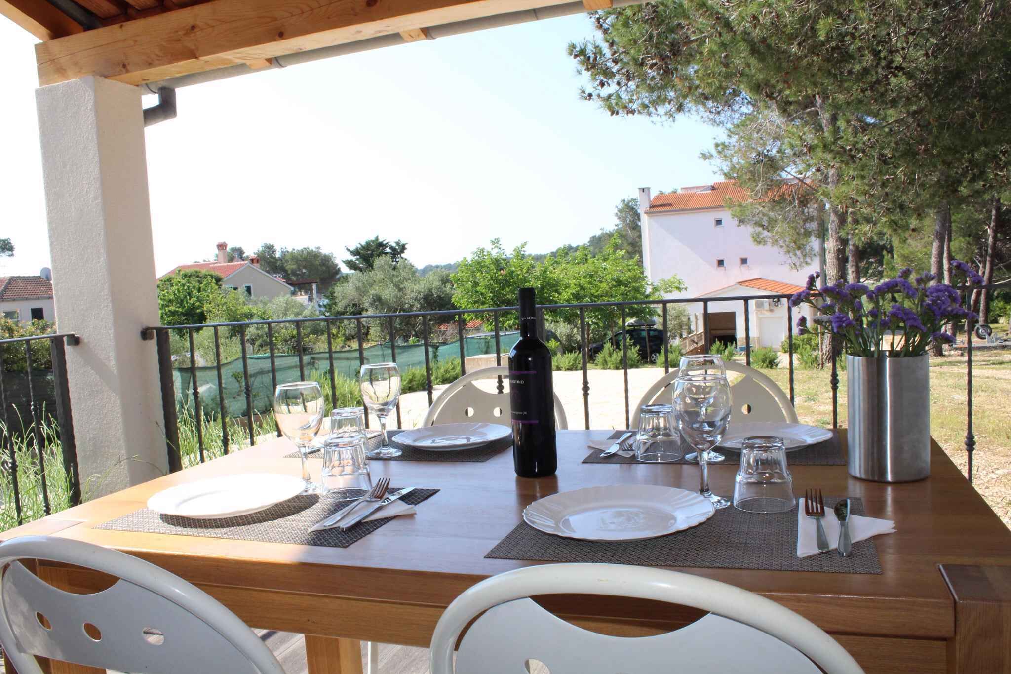 An outdoor dining table set with plates, cutlery, and a bottle, surrounded by chairs and a metal railing.
