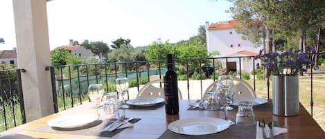 An outdoor dining table set with plates, cutlery, and a bottle, surrounded by chairs and a metal railing.