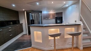A modern kitchen with dark cabinets, a stainless steel refrigerator, and a central island with bar stools. - Apartment at the foot of Cannes Port of 70m2 (Cannes)