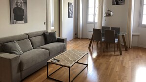 A modern living room with a grey sofa, a glass coffee table, and a dining area with chairs and a table. - Apartment at the foot of Cannes Port of 70m2 (Cannes)