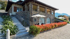 A stone building with a balcony, a staircase, and outdoor seating with umbrellas. - Agriturismo Il Colle (Bellagio)