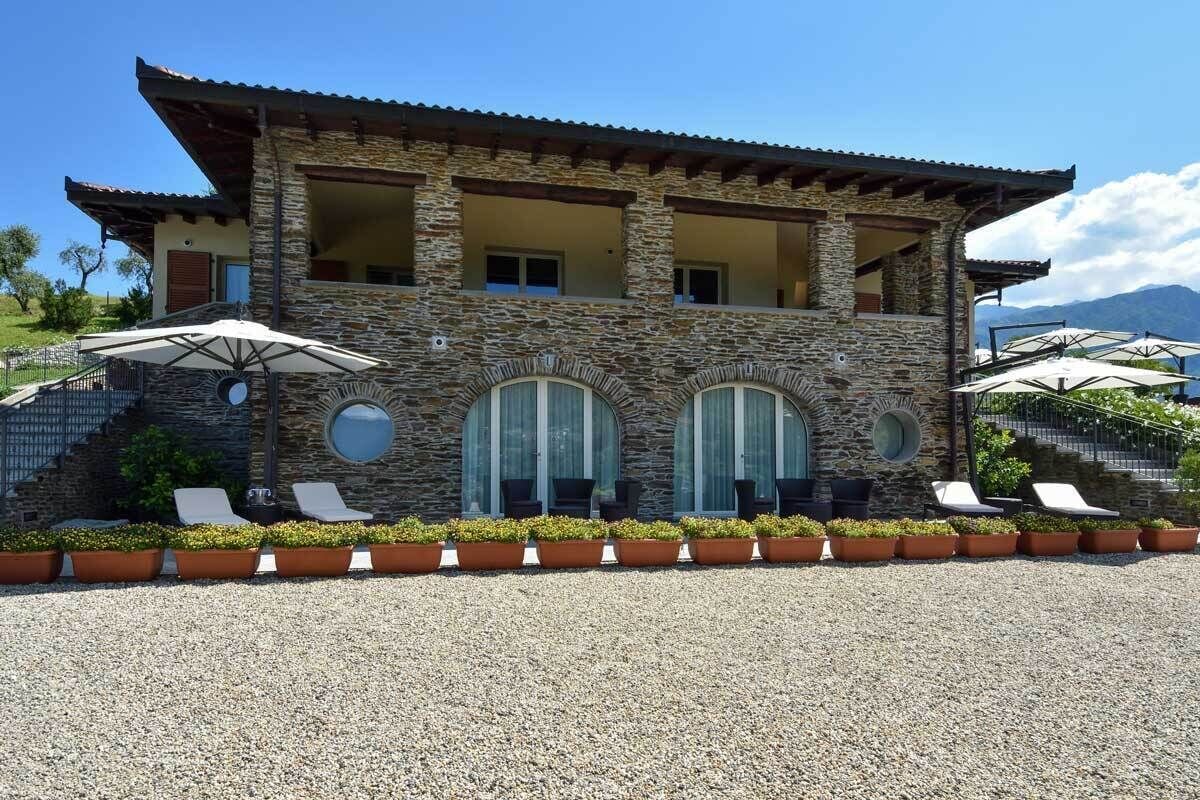 A two-story stone building with a balcony, outdoor seating with umbrellas, and a gravel driveway.