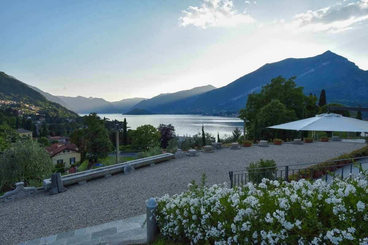 Une terrasse offrant une vue sur un lac et des montagnes, entourée de verdure et agrémentée de plantes en pot.