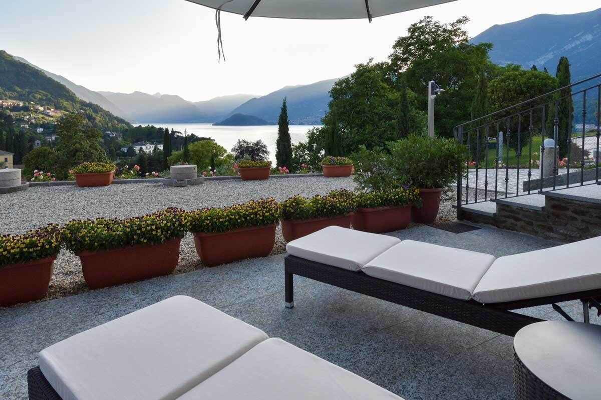 Una terrazza con poltrone e piante in vaso, vista su un lago e montagne.