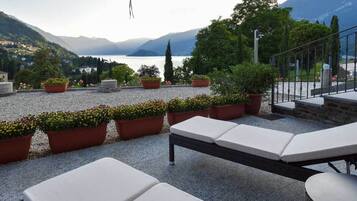 Terraza con sillones de descanso y plantas en macetas, con vistas a un lago y montañas.