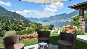 A patio with wicker chairs, a table, and a view of a lake and mountains. - Agriturismo Il Colle (Bellagio)