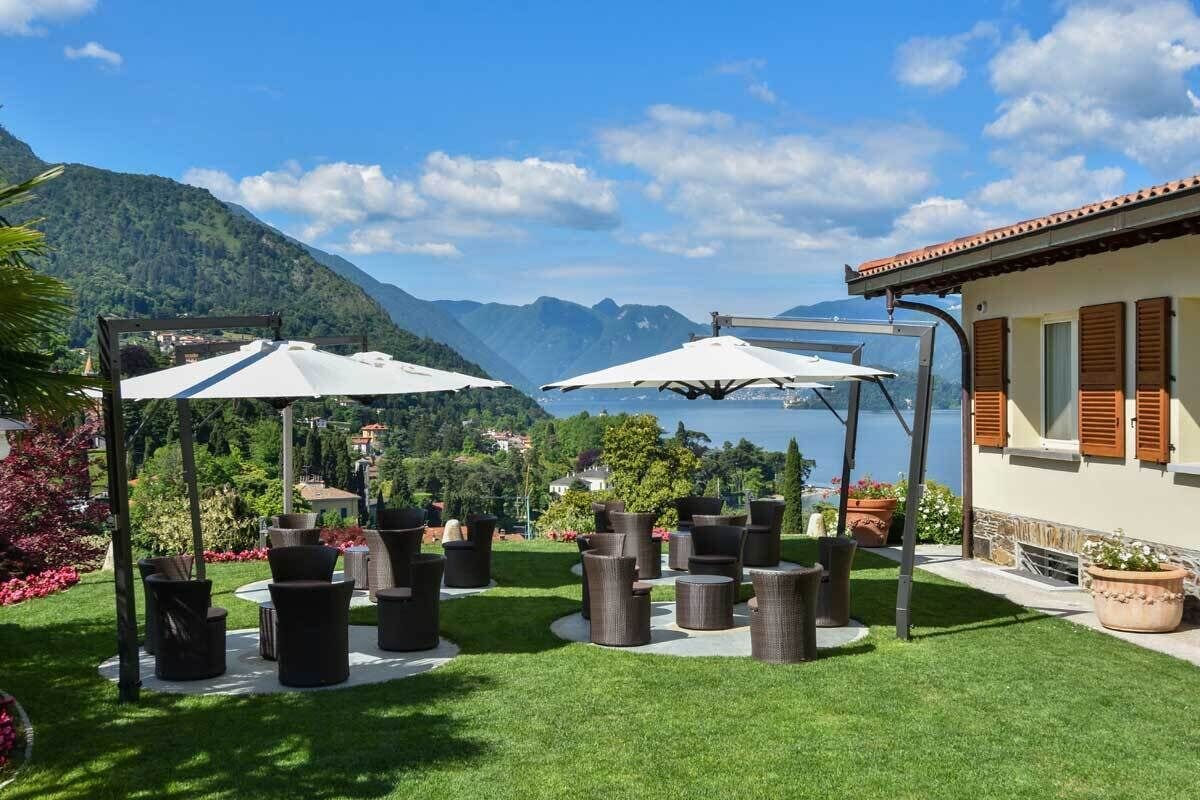 Un patio con mobiliario exterior y sombrillas, con vista a un lago y montañas.