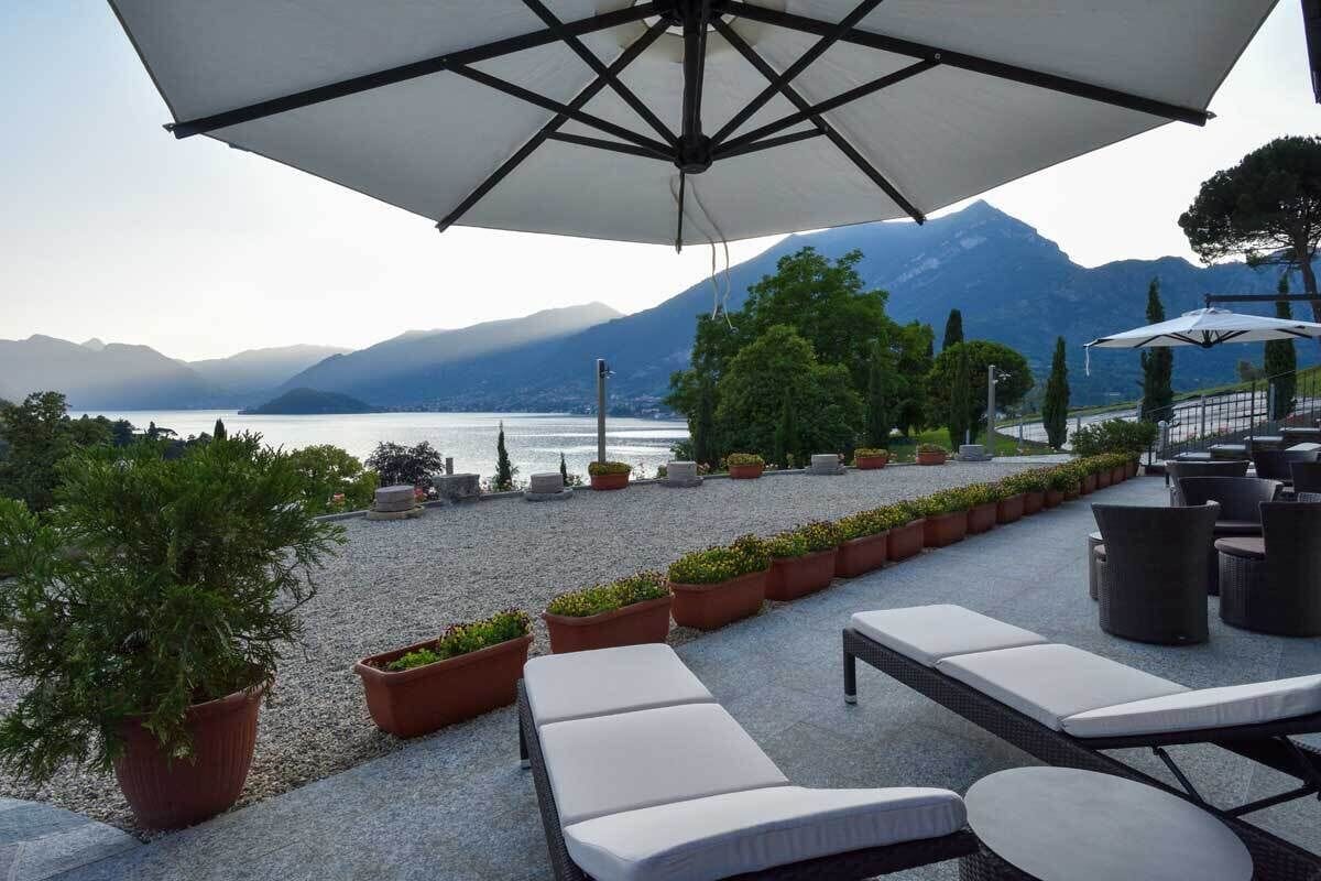 Una terrazza con poltrone e piante in vaso, vista su un lago e montagne.