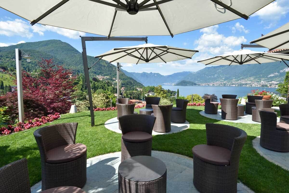 Ein Sitzbereich im Freien mit Korbmöbeln und Sonnenschirmen mit Blick auf einen See und Berge.