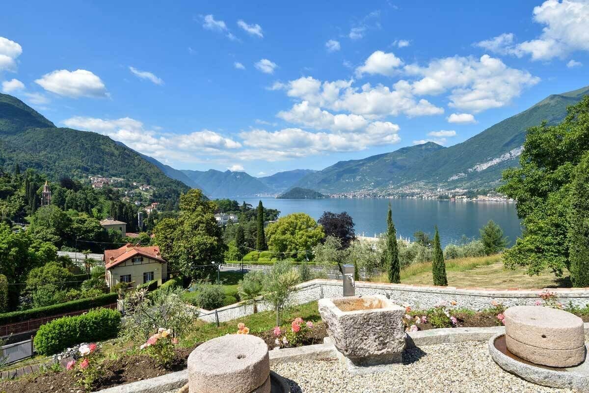 Une vue pittoresque d’un lac, avec des montagnes en arrière-plan, une petite maison avec un toit rouge et des constructions en pierre au premier plan.