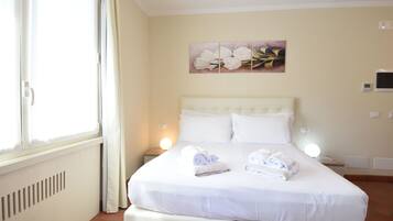 Una cama bien hecha con toallas, cabecero blanco y una obra de arte colgada en la pared.