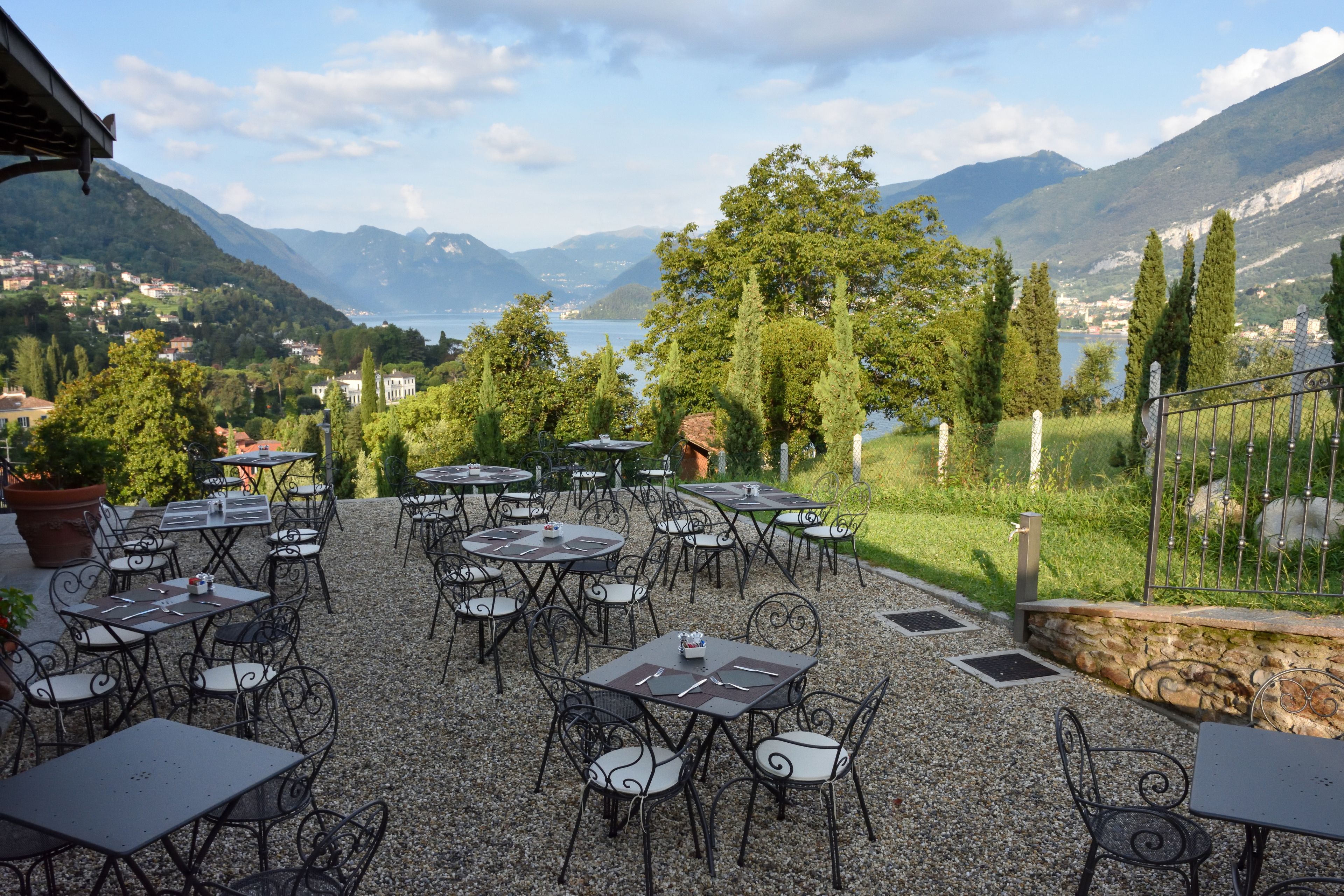 Eine Terrasse im Freien mit Tischen und Stühlen, mit Blick auf einen See und Berge.