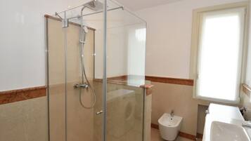 Een moderne badkamer met een douche met glazen wand, een toiletbrons en een wastafel.