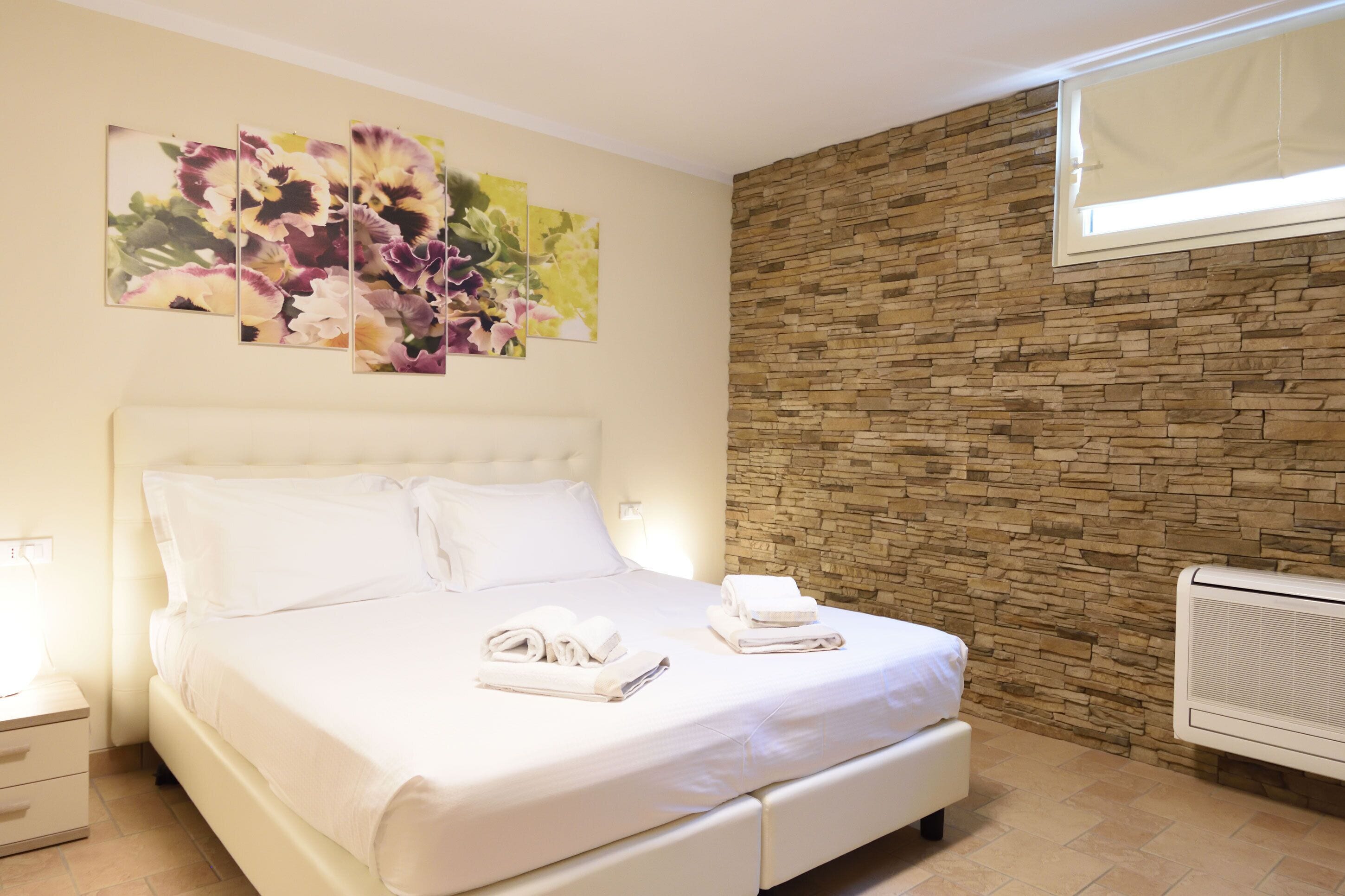Una cama bien hecha con ropa de cama y toallas blancas, una pared de piedra y una ventana con persianas.