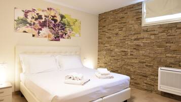Una cama bien hecha con ropa de cama y toallas blancas, una pared de piedra y una ventana con persianas.
