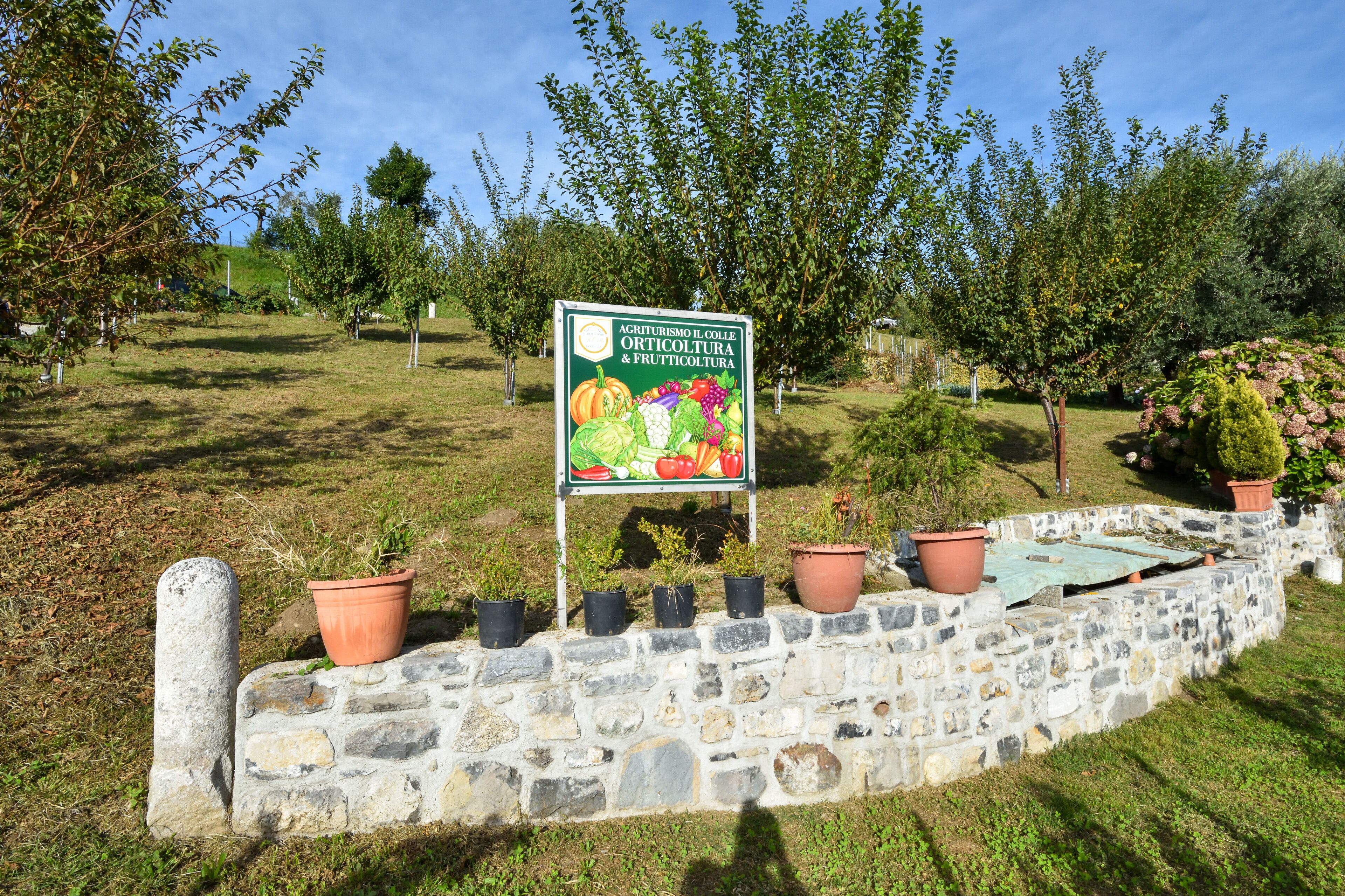 A stone wall with potted plants and a sign about agriturismo.