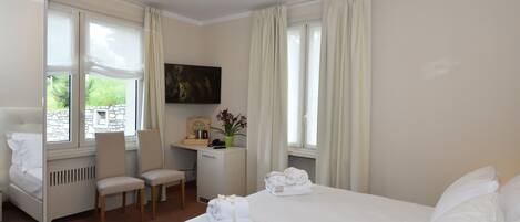 A hotel room with a bed, two chairs, a desk, a TV, and a window with curtains.