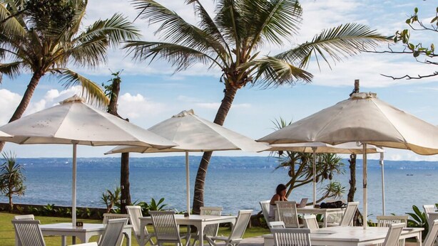 Un espace extérieur aménagé avec des tables et des chaises sous des parasols, offrant une vue sur une étendue d’eau.