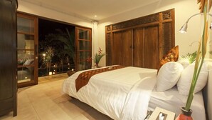 Une chambre avec un grand lit, une armoire en bois et un balcon agrémenté de plantes.