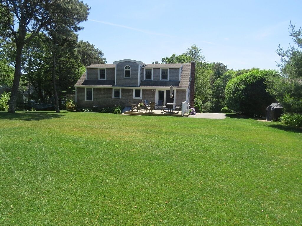 A two-story house with a front porch, a lawn, and a patio area with outdoor furniture.