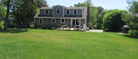 A two-story house with a front porch, a lawn, and a patio area with outdoor furniture.