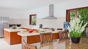 Una cocina moderna con una isla central, sillas de madera, una mesa de vidrio y una planta en maceta.