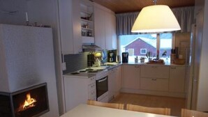 A cozy kitchen with a wood-burning stove, a dining table with a candle, and a view of a house through the window. - Rantala by Interhome (Suonenjoki)