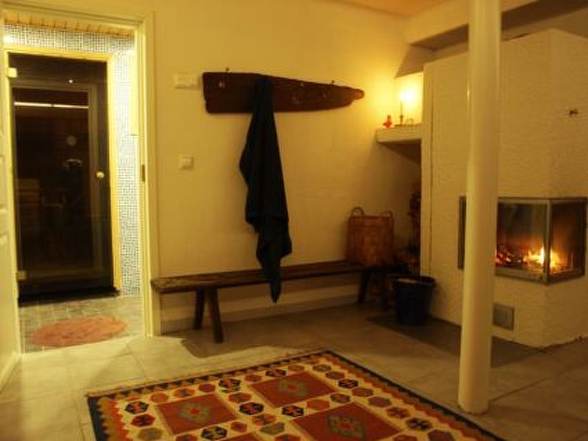 Un pasillo con alfombra estampada, un banco, perchero y chimenea.