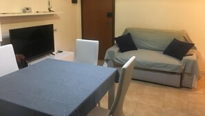 Ein Wohnzimmer mit einer Couch, einem Fernseher, einem Tisch und einer Tür.