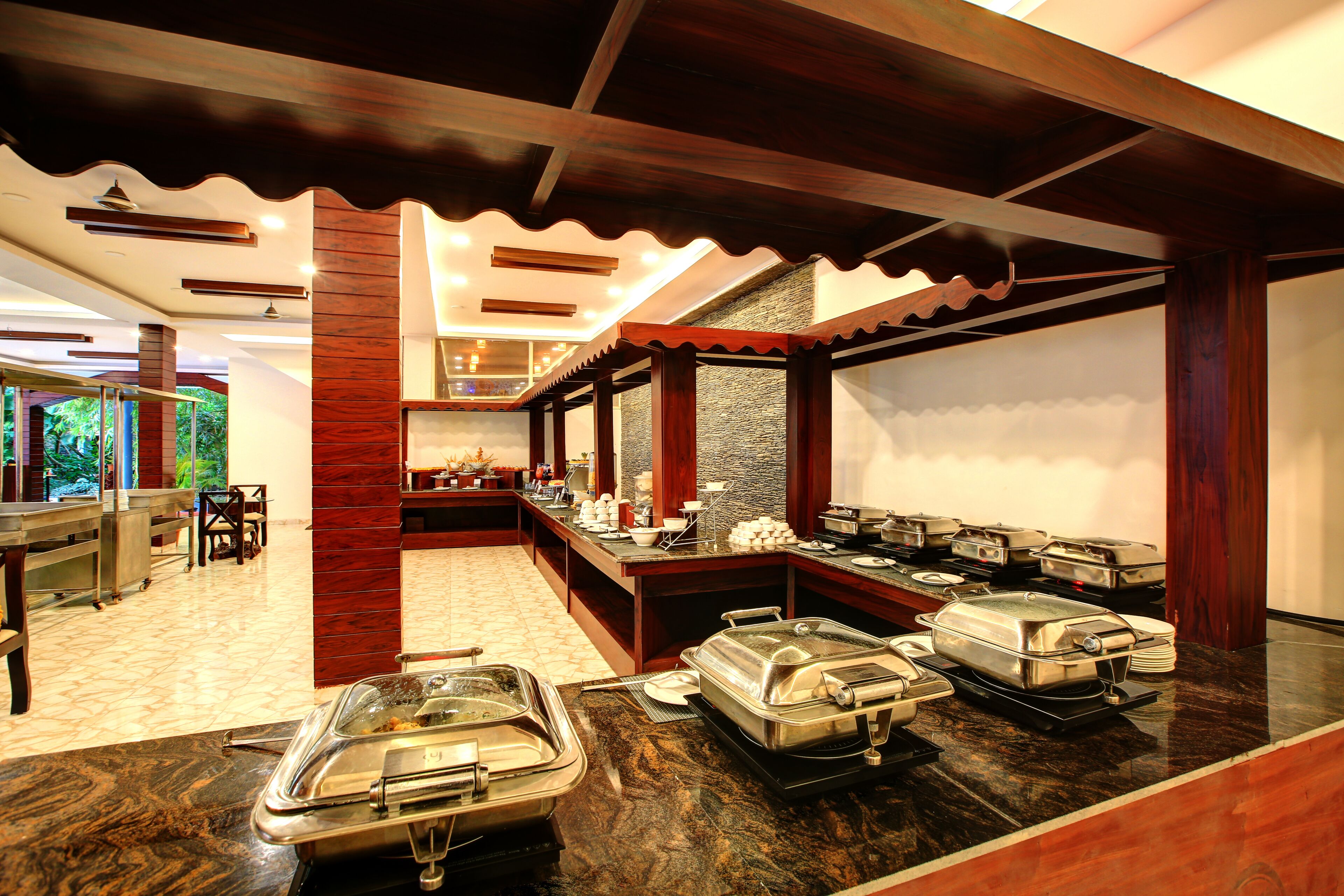 A buffet area with multiple serving stations, a marble countertop, and a high ceiling with wooden beams.