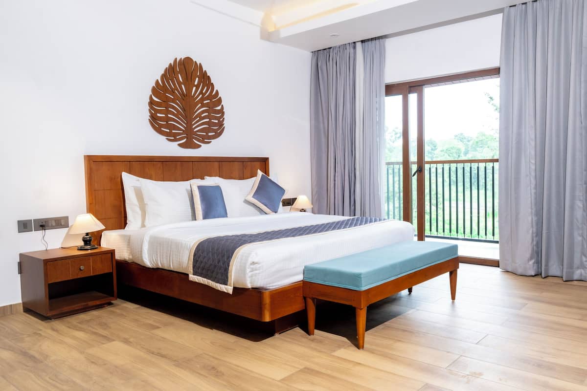 Quarto moderno com cama de madeira, um banco, mesa de cabeceira e uma janela grande com cortinas.