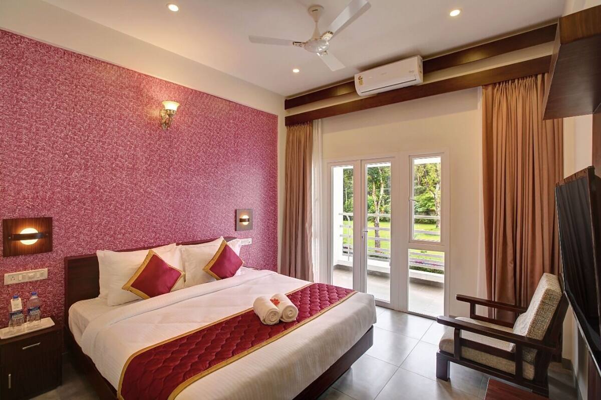 Quarto de hotel com uma cama grande, ventoinha no teto, ar condicionado, mesa de cabeceira com artigos de higiene pessoal e vista para o exterior através de uma porta de correr.