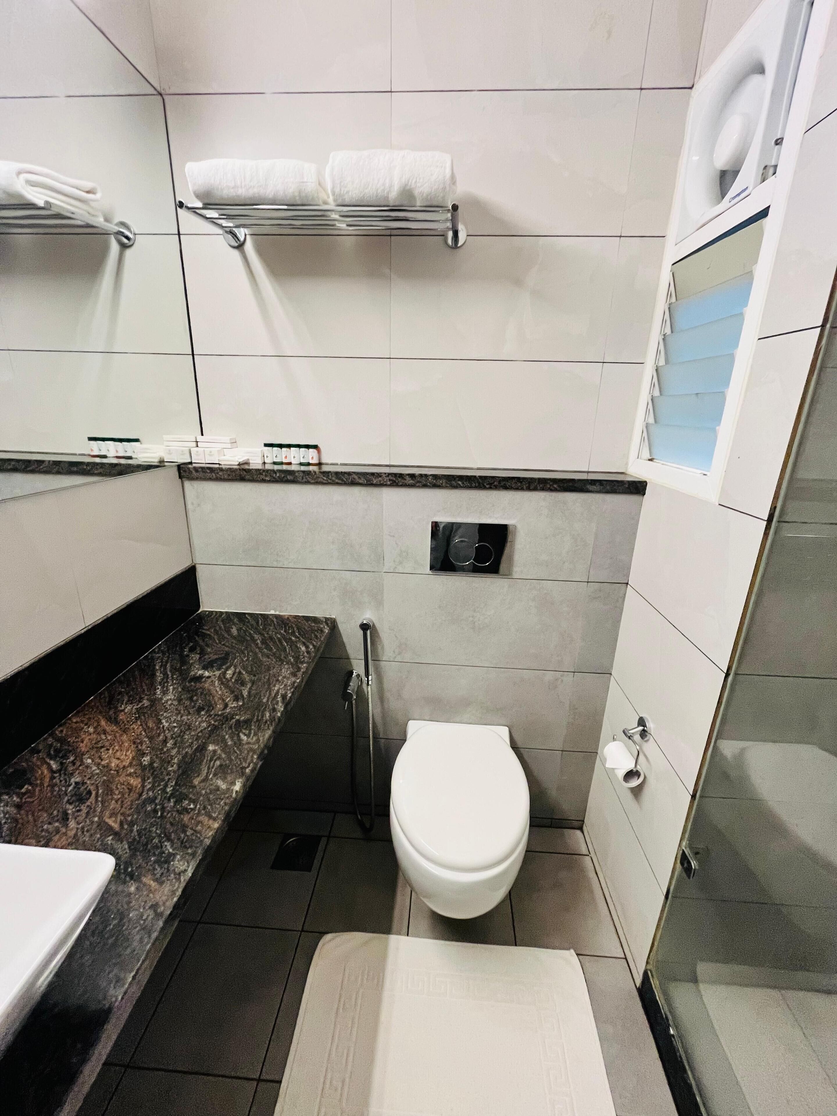Une salle de bain moderne avec un plan de toilette en marbre, des toilettes, un porte-serviettes et une douche.