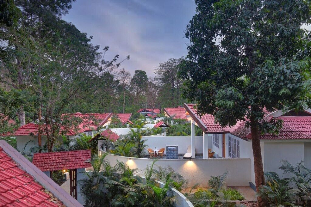 A resort with multiple buildings, each with a red-tiled roof, surrounded by lush greenery and palm trees.