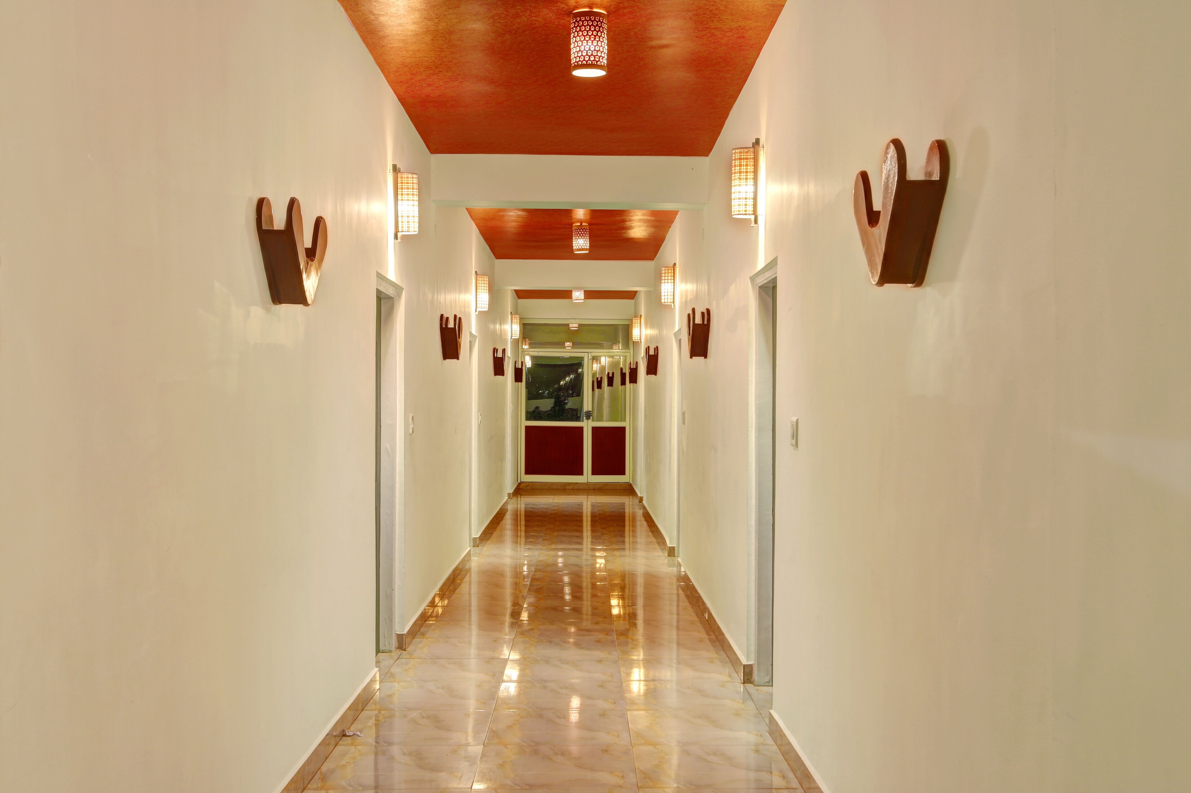 A hallway with a polished marble floor, wooden ceiling, and wall-mounted light fixtures.