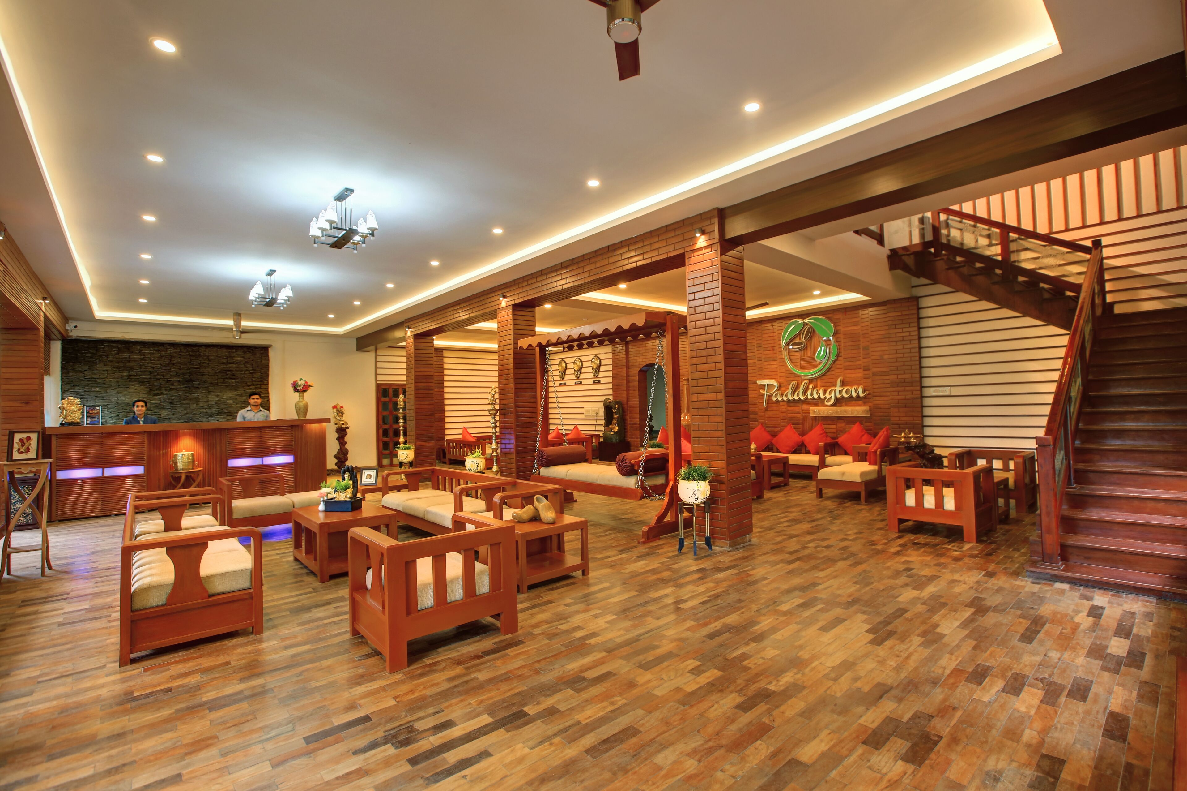 A spacious lobby with wooden flooring, multiple seating areas, a reception desk, and a staircase.