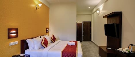 Une chambre d’hôtel équipée d’un lit, d’une table de chevet, d’une lampe, d’une télévision et d’un ventilateur de plafond.
