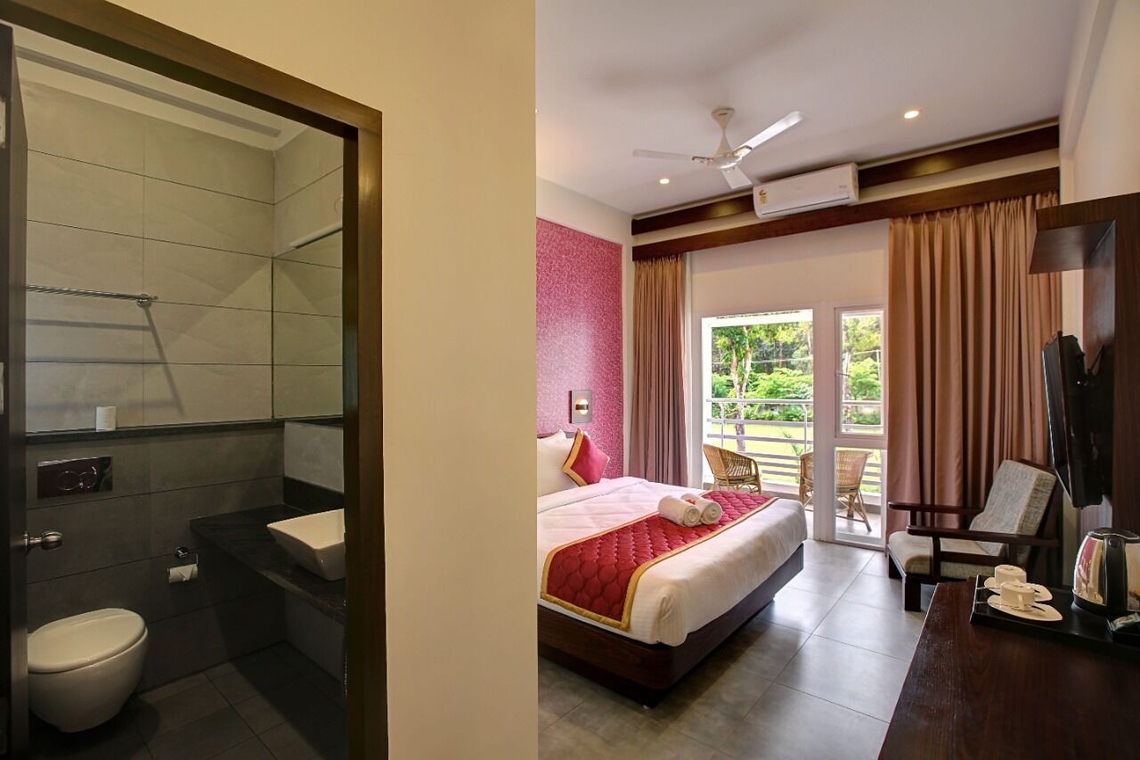 Habitación de hotel con ducha, inodoro, cama y balcón con una silla.
