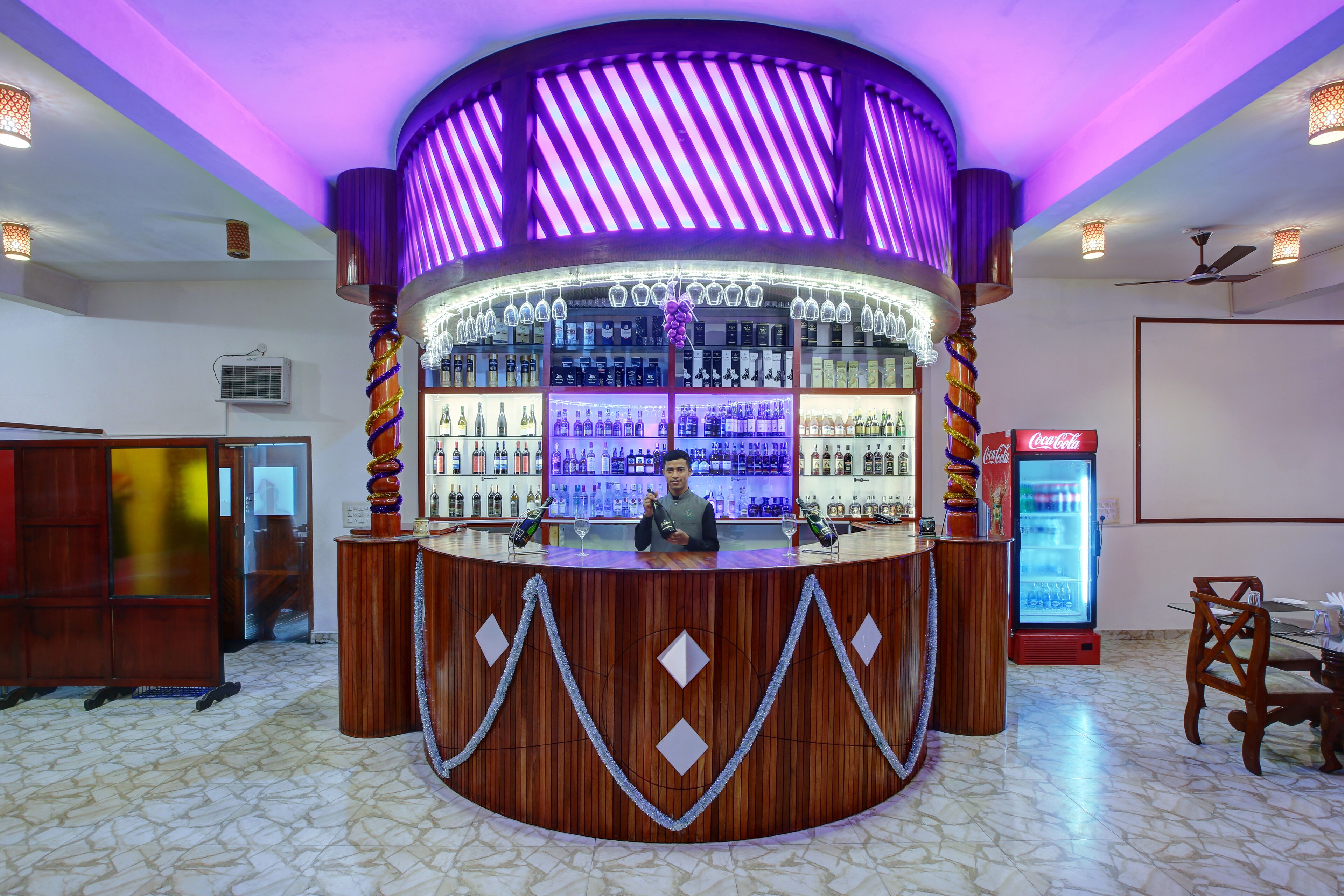 Eine Bar mit einer runden Holztheke, Regalen mit Flaschen und einem Coca-Cola-Kühlschrank.