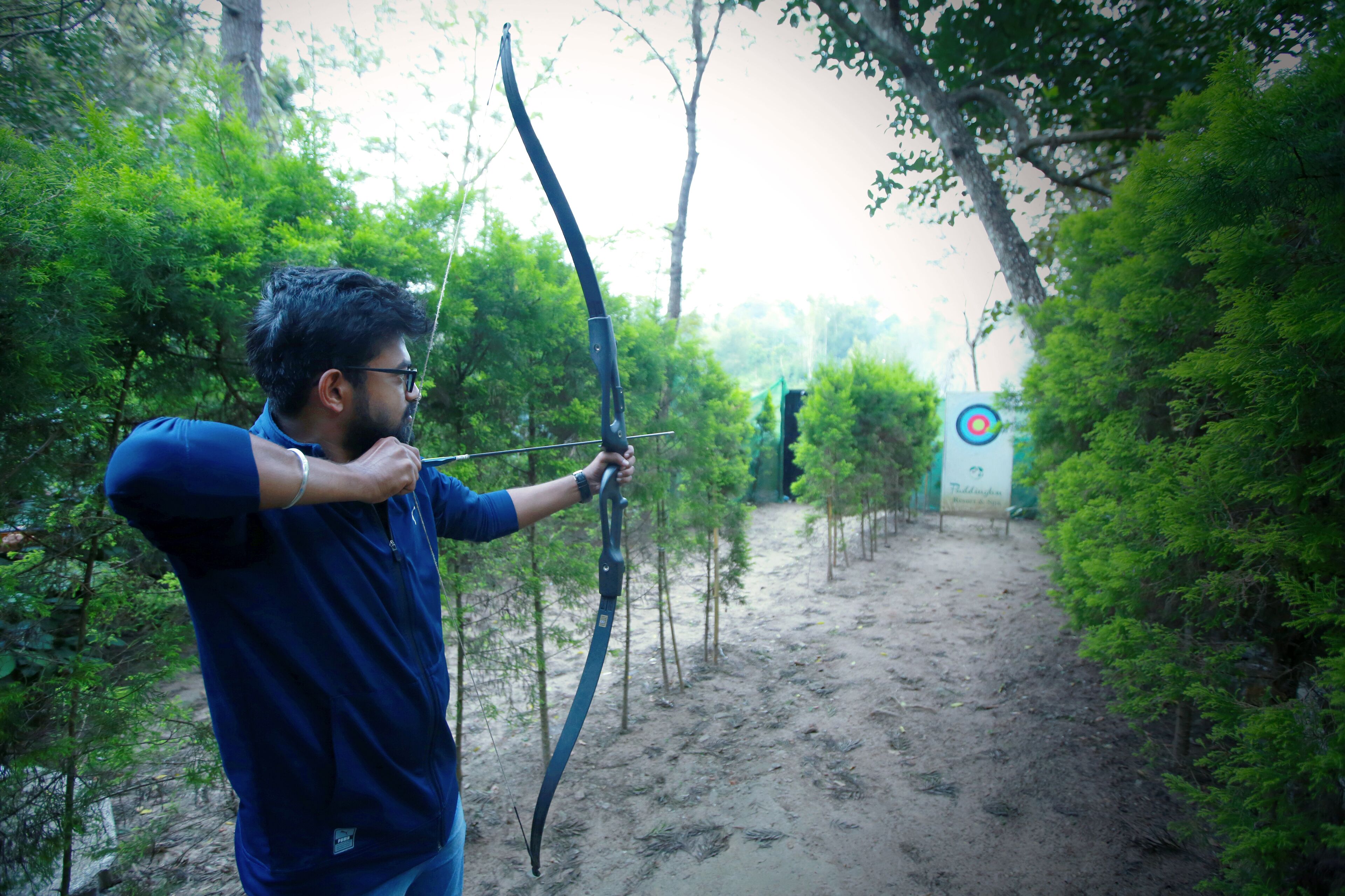 A person aiming a bow in a forested area.