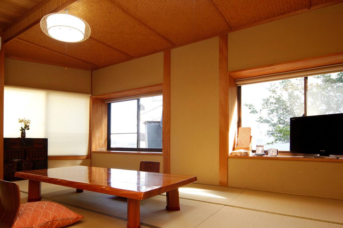 A traditional Japanese room with tatami flooring, a wooden table, a television, and a window with a view.