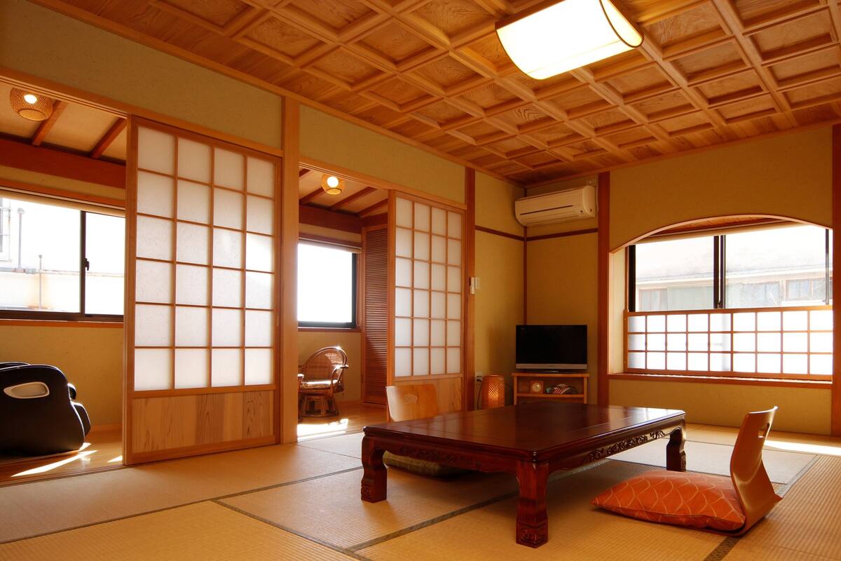 A traditional Japanese room with tatami flooring, a low wooden table, a television, and sliding doors.