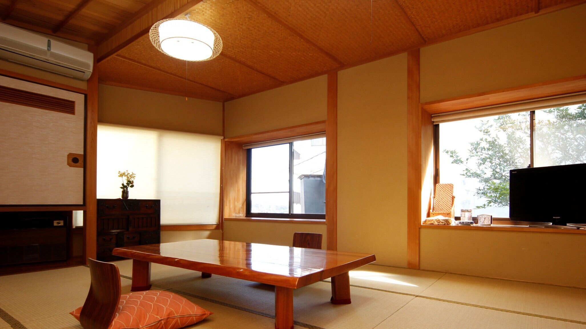 A traditional Japanese room with tatami flooring, a wooden table, a television, and a window with a view of greenery.