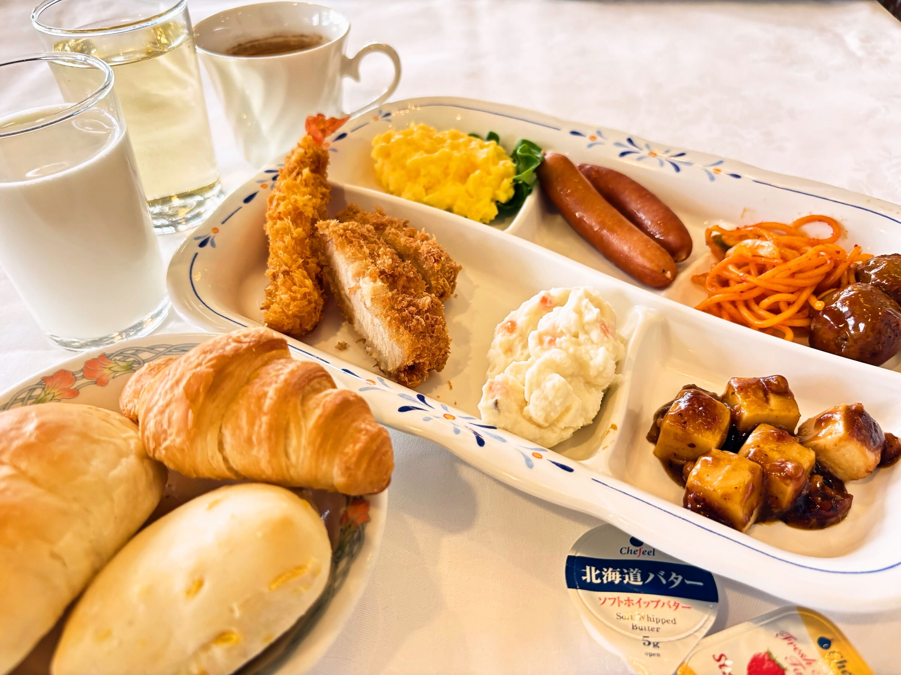 Bandeja de desayuno con cruasanes, salchichas, huevos revueltos y guarnición de verduras.