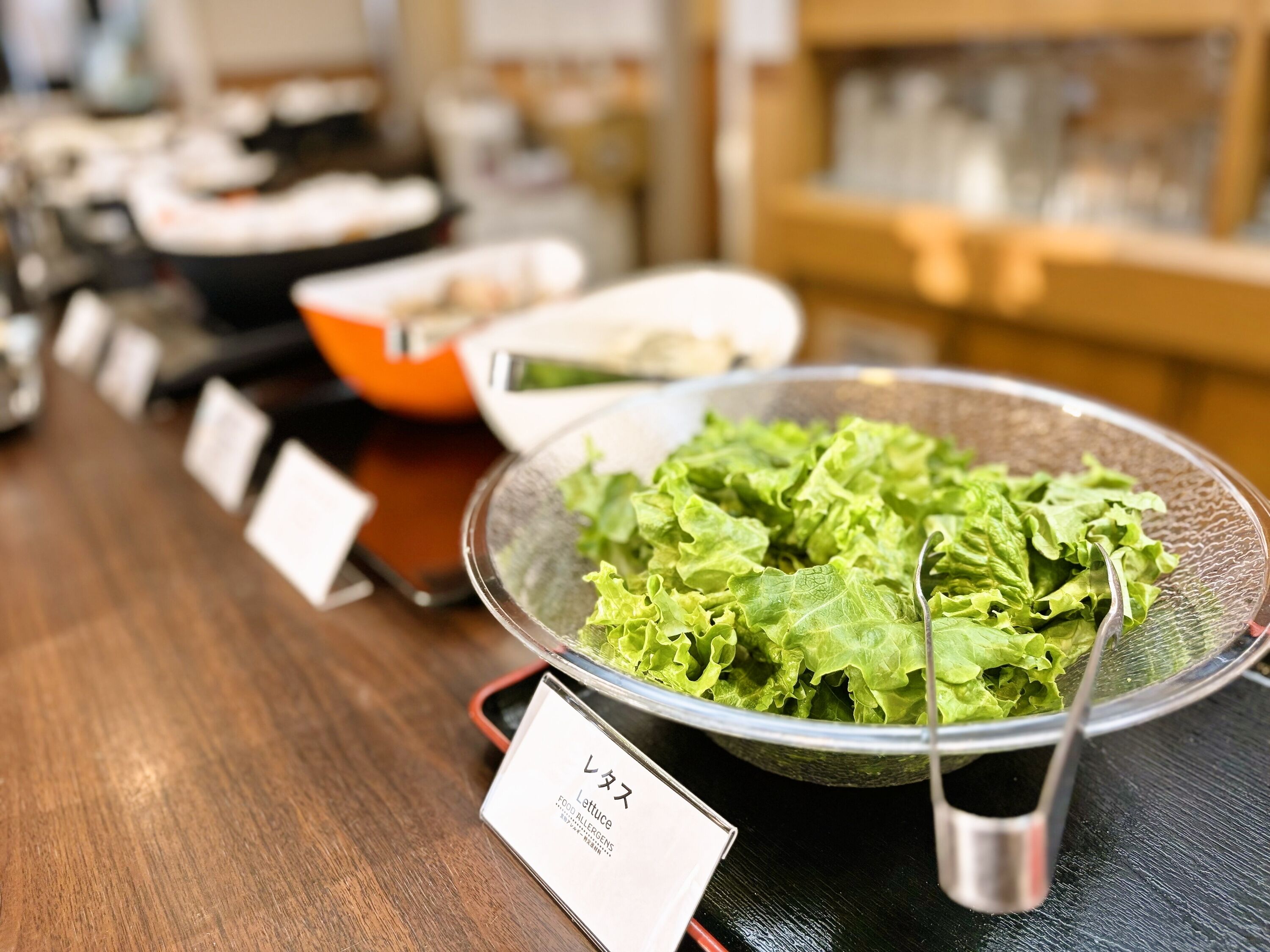 A salad bar with various dishes and a sign indicating lettuce is a food allergen.